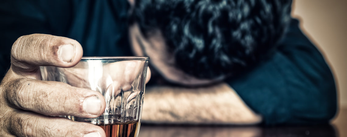 Depressed drunk man holding a drink and sleeping with his head on the table  (Focused on the drink, his face is out of focus)