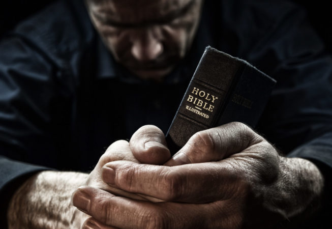 A Man praying holding a Holy Bible.