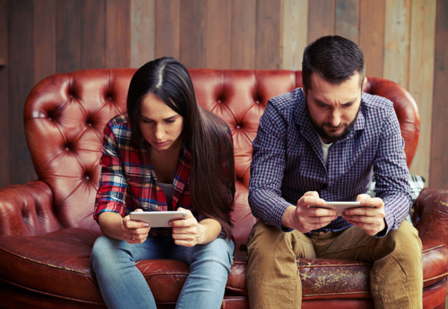 concept photo of smartphone addiction. young woman and man sitting on the sofa with smartphone and do not looking at each other